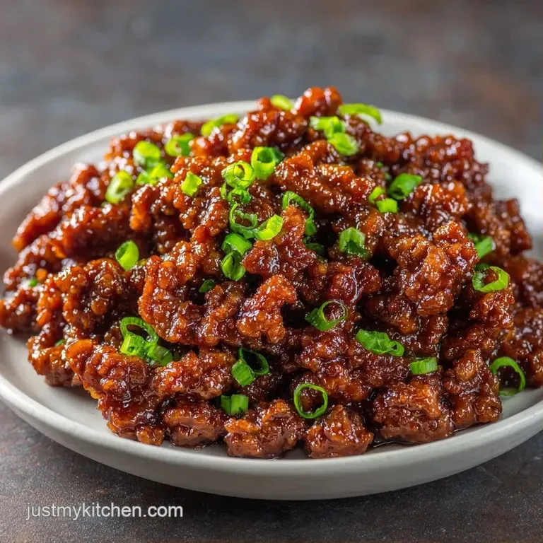 A white ceramic bowl filled with glossy browned beef and sliced green onions, garnished with toasted sesame seeds.