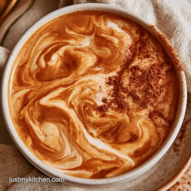 Chilled coffee with creamy swirls in a tall glass, paired with a cinnamon stick and golden syrup on a wooden surface.