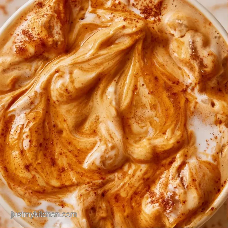 A tall glass of iced coffee with a marbled orange cream swirl, set on a rustic wooden coaster with autumn leaves.
