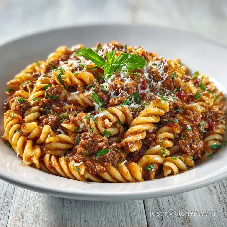 Elegant portion of beefy pasta topped with gooey melted cheese and fresh herbs on a clean white ceramic plate.