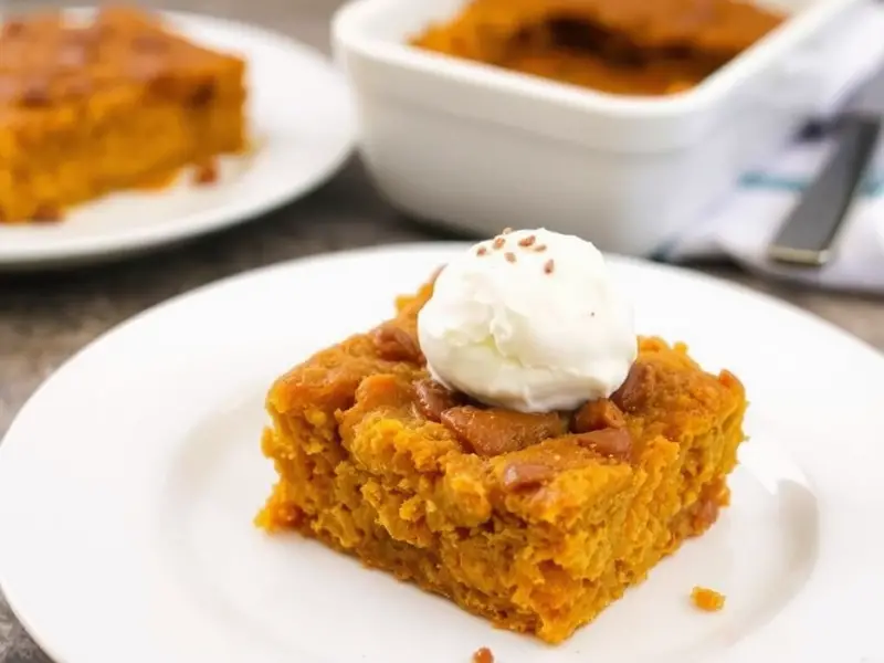 A serving of pumpkin dump cake with a golden crumble topping, served on a plate and garnished with whipped cream and cinnamon.